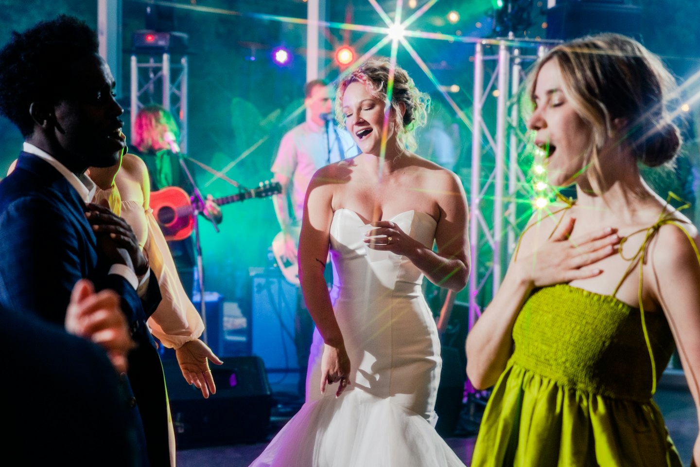 Hochzeitsgäste tanzen und singen fröhlich in der Nähe einer Braut in einem weißen Kleid.